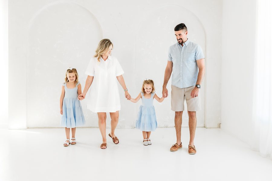 Parents and two daughters holding hands across the bright white studio