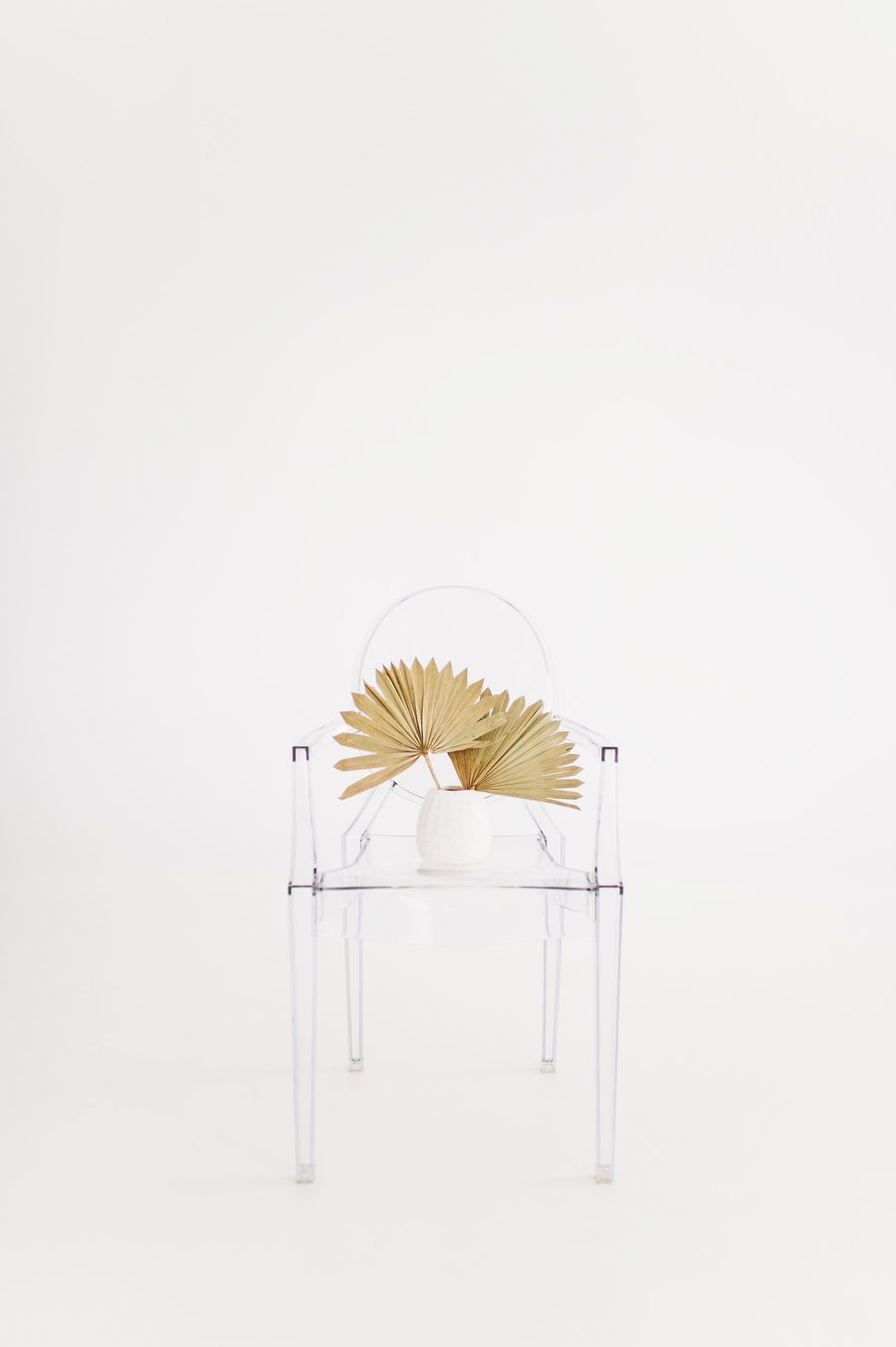 A clear chair with a woven fan against a white wall