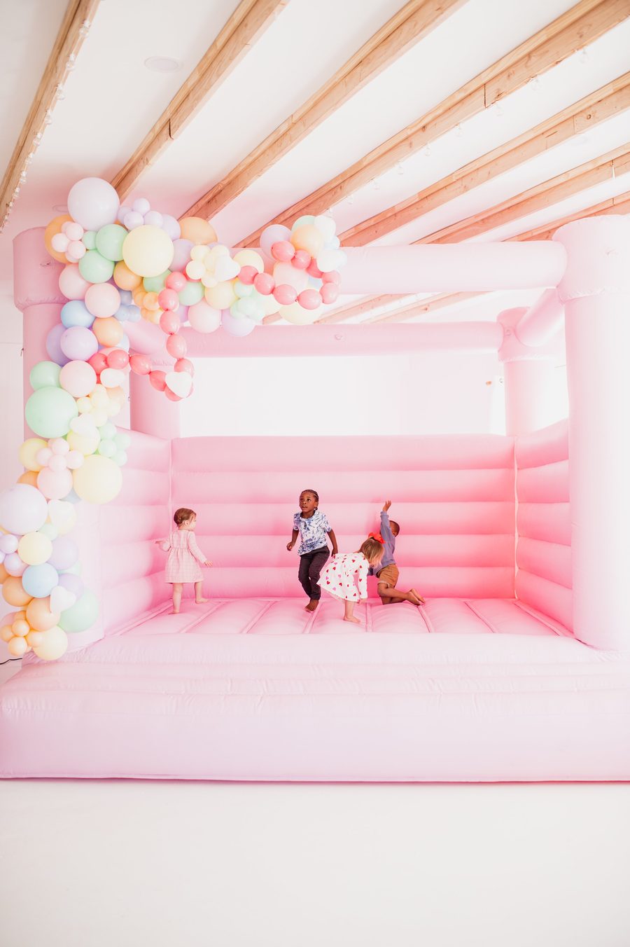 Children in a pastel pink bounce house under a balloon arch