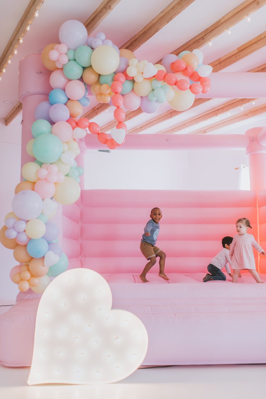 A pink bounce house with a pastel balloon garland