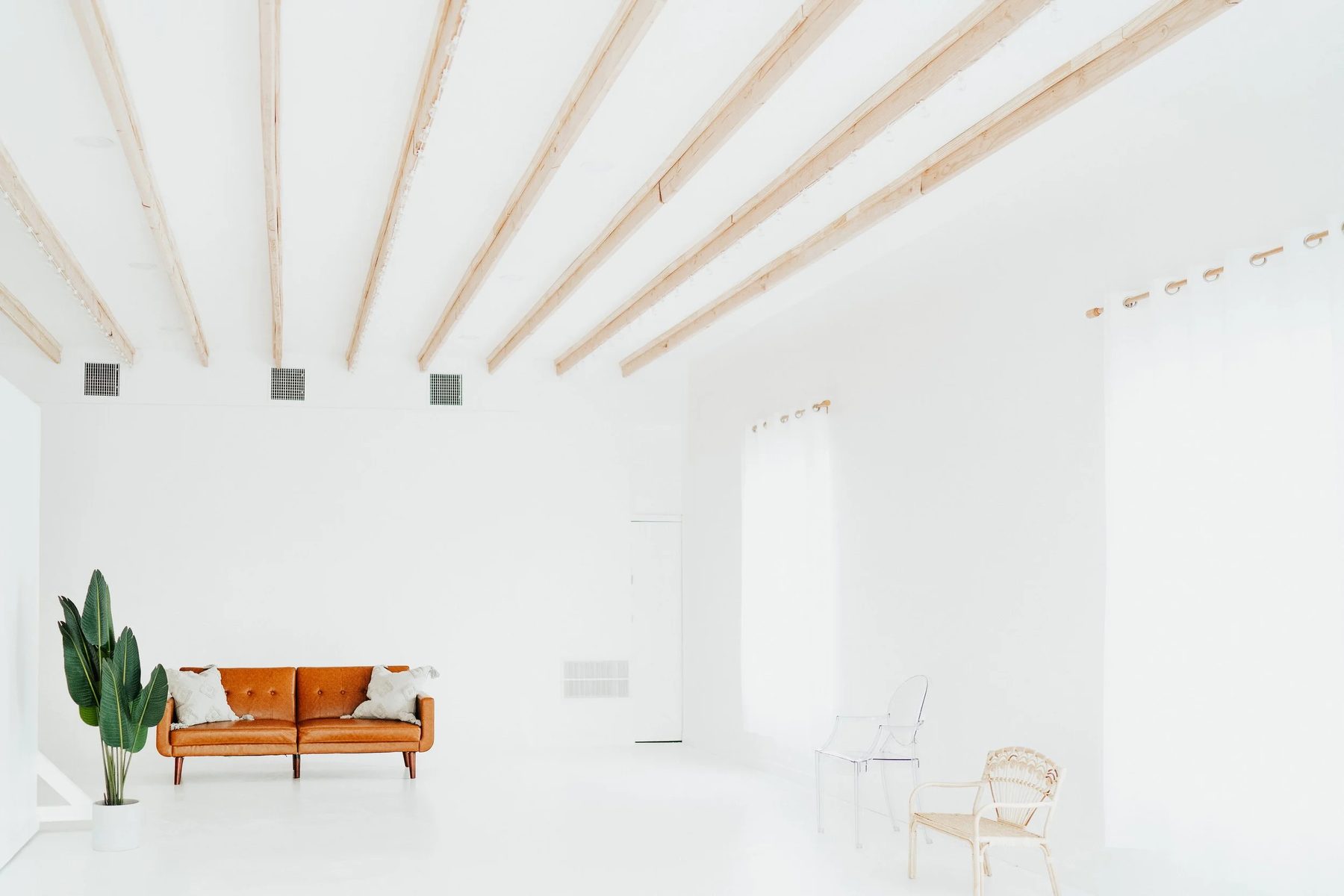 Ren studio — white room with wood-beam ceiling and a leather sofa in natural light